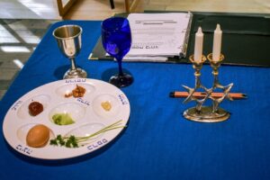 Seder plate, kiddush cup, Miriam's cup, and candlesticks together with a Passover Haggadah on a blue tablecloth