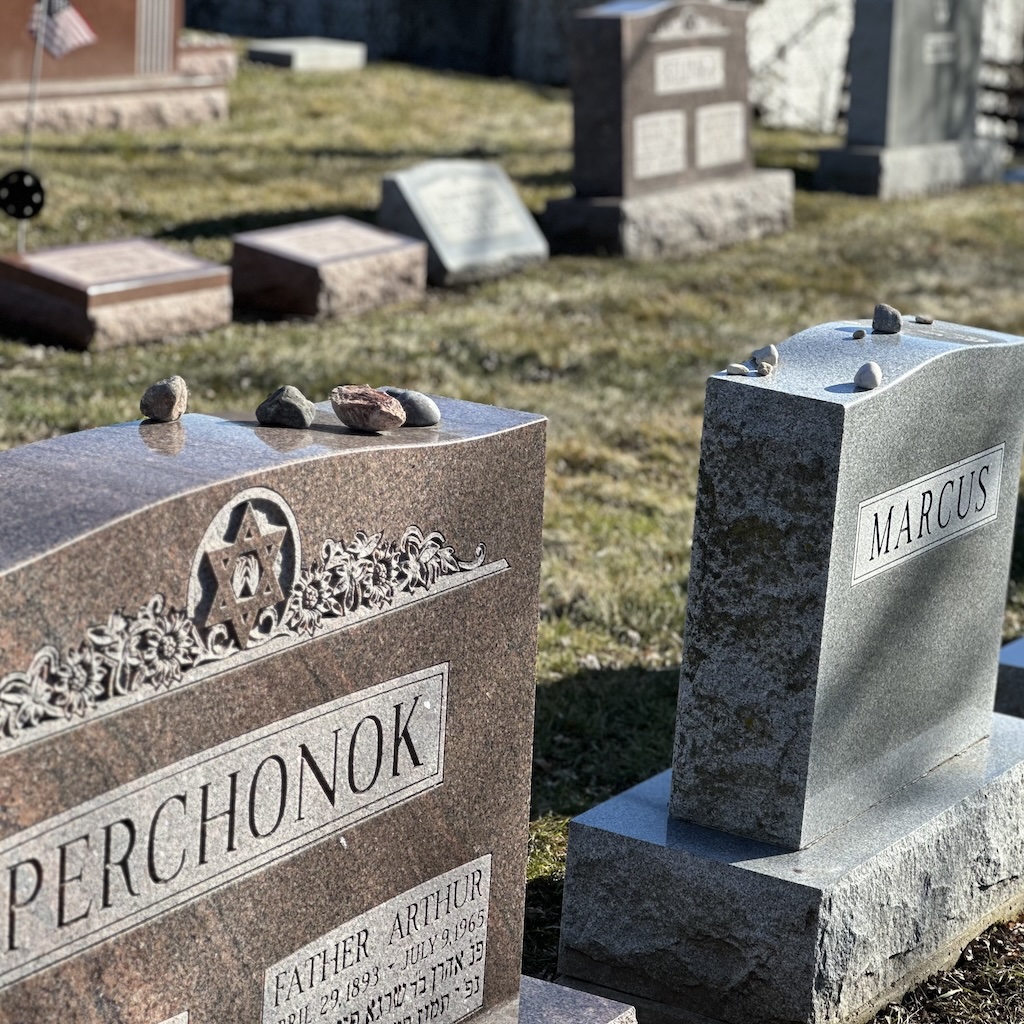 Jewish headstones in a cemetery with visitation stones placed on top of the headstones